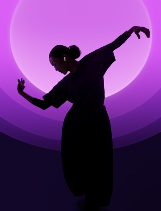 Une personne danse avec ses AirPods 5 aux oreilles, sur fond multicolore