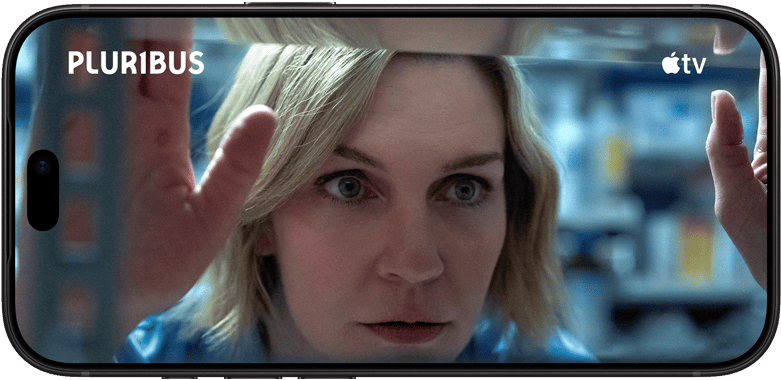 iPhone 18 Pro, mode paysage, affichant un gros plan d’une femme regardant à travers une étagère. Nom de la série : Pluribus
