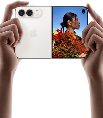 iPhone Duo, finition blanc stellaire, tenu à deux mains en position horizontale, déplié, le volet extérieur gauche présente les caméras arrière Fusion 48 MP, le volet extérieur droit présente l’écran externe affichant une personne qui se fait photographier et peut voir son propre visage pendant la prise de vue à l’aide de Duo Preview