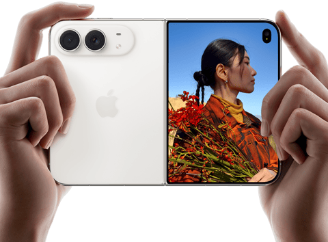 iPhone Duo, finition blanc stellaire, tenu à deux mains en position horizontale, déplié, le volet extérieur gauche présente les caméras arrière Fusion 48 MP, le volet extérieur droit présente l’écran externe affichant une personne qui se fait photographier et peut voir son propre visage pendant la prise de vue à l’aide de Duo Preview