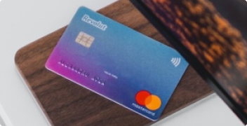 une carte bancaire Mastercard de la marque Revolut posée sur un support en bois