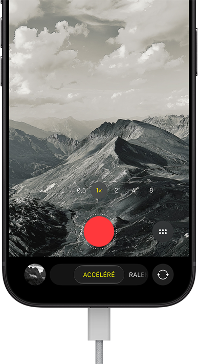 iPhone 18 Pro, face avant, affichant un paysage                                                                montagneux, avec le mode caméra incrusté en mode                                                                Accéléré, avec câble d’alimentation branché sur le port                                                                de charge
