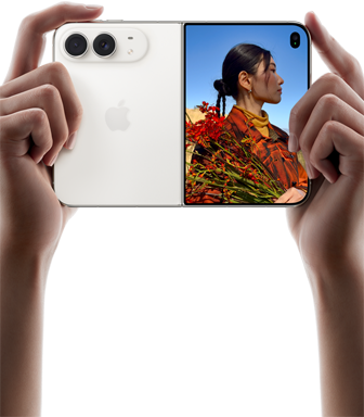 iPhone Duo,                                                                finition blanc stellaire, tenu à deux mains en position                                                                horizontale, déplié, le volet extérieur gauche présente                                                                les caméras arrière Fusion 48 MP, le volet extérieur                                                                droit présente l’écran externe affichant une personne                                                                qui se fait photographier et peut voir son propre visage                                                                pendant la prise de vue à l’aide de Duo Preview