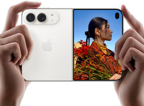 iPhone Duo, finition blanc stellaire, tenu à deux                                                                mains en position horizontale, déplié, le volet                                                                extérieur gauche présente les caméras arrière Fusion 48                                                                MP, le volet extérieur droit présente l’écran externe                                                                affichant une personne qui se fait photographier et peut                                                                voir son propre visage pendant la prise de vue à l’aide                                                                de Duo Preview