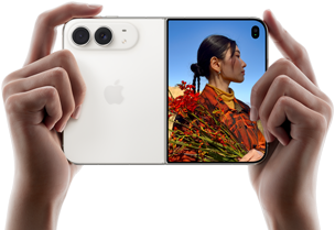 iPhone Duo,                                                                finition blanc stellaire, tenu à deux mains en position                                                                horizontale, déplié, le volet extérieur gauche présente                                                                les caméras arrière Fusion 48 MP, le volet extérieur                                                                droit présente l’écran externe affichant une personne                                                                qui se fait photographier et peut voir son propre visage                                                                pendant la prise de vue à l’aide de Duo Preview